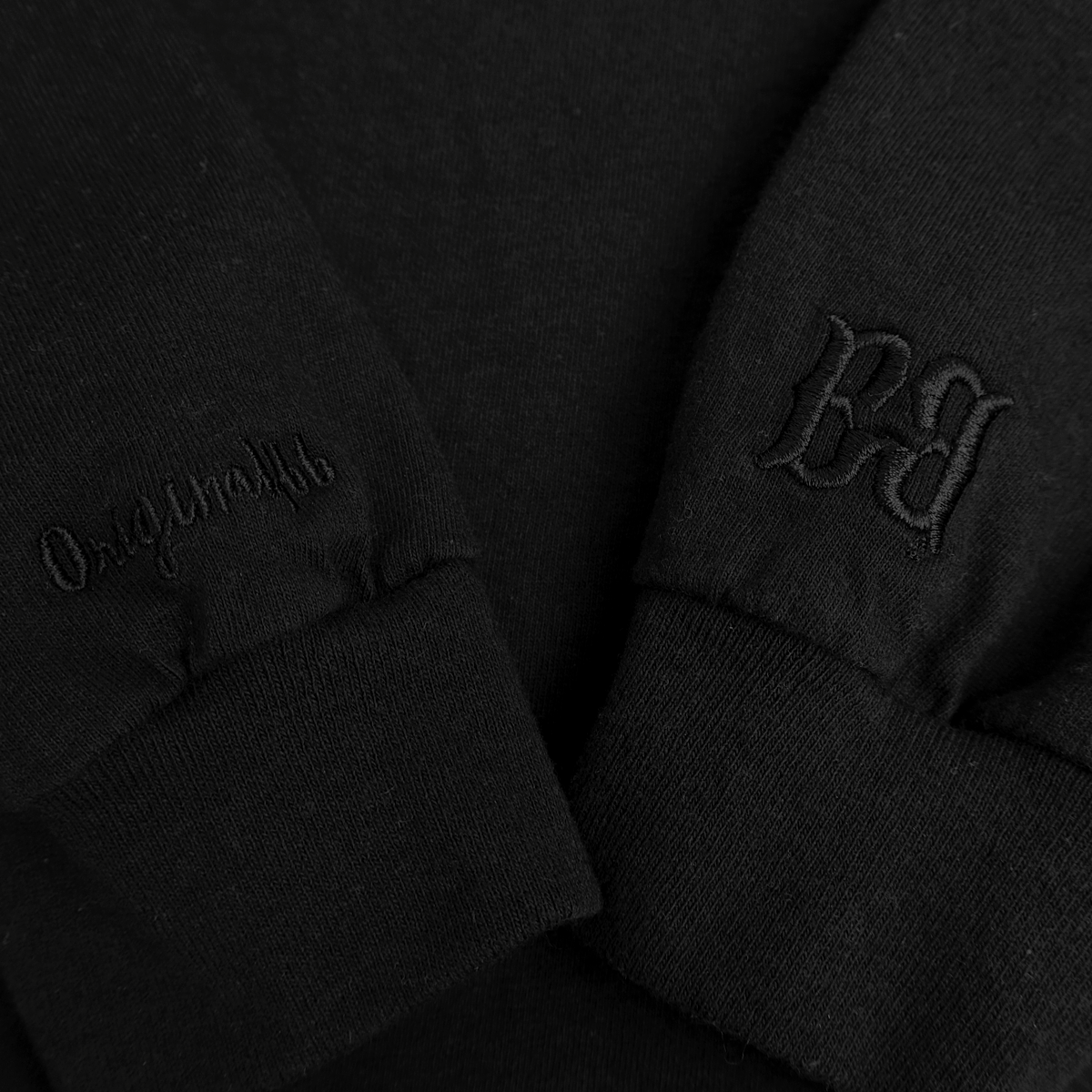 Close-up of black FBB long-sleeve tee cuffs with tonal Originalfbb script embroidery and an FBB monogram.