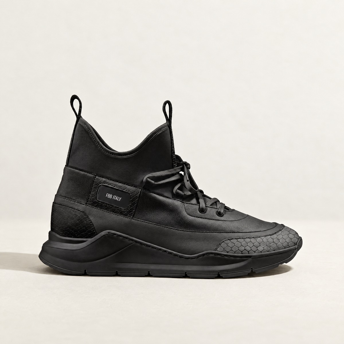 A black mid-top athletic sneaker with a textured leather and suede upper, black laces featuring a python embossed toe box and a chunky black sole, shown in profile against a light off-white background.