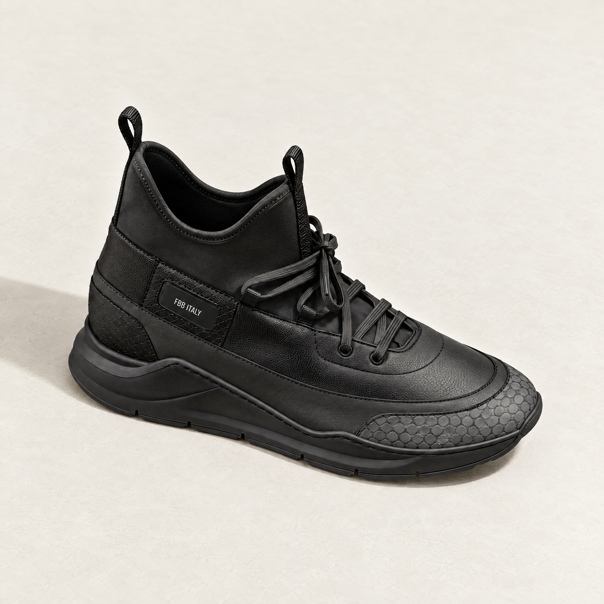 A three-quarter view of a black mid-top athletic sneaker with a textured leather and suede upper, black laces featuring a python embossed toe box and a chunky black sole.