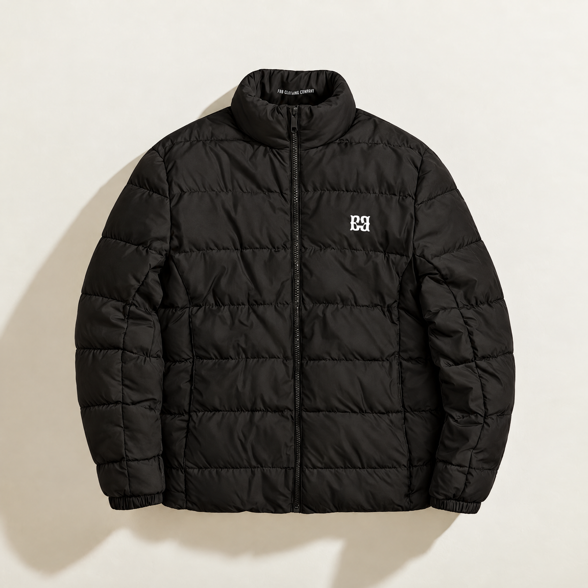 Front view of the black FBB puffer jacket with horizontal quilting, a stand collar and white chest monogram.