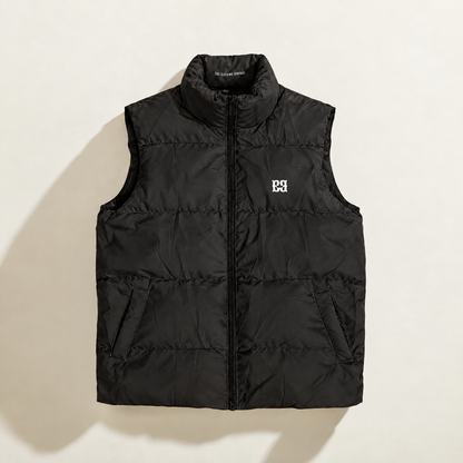 A black sleeveless down puffer vest with a stand-up collar and front zipper, featuring a small white embroidered monogram logo on the left chest, displayed flat against a light beige background.