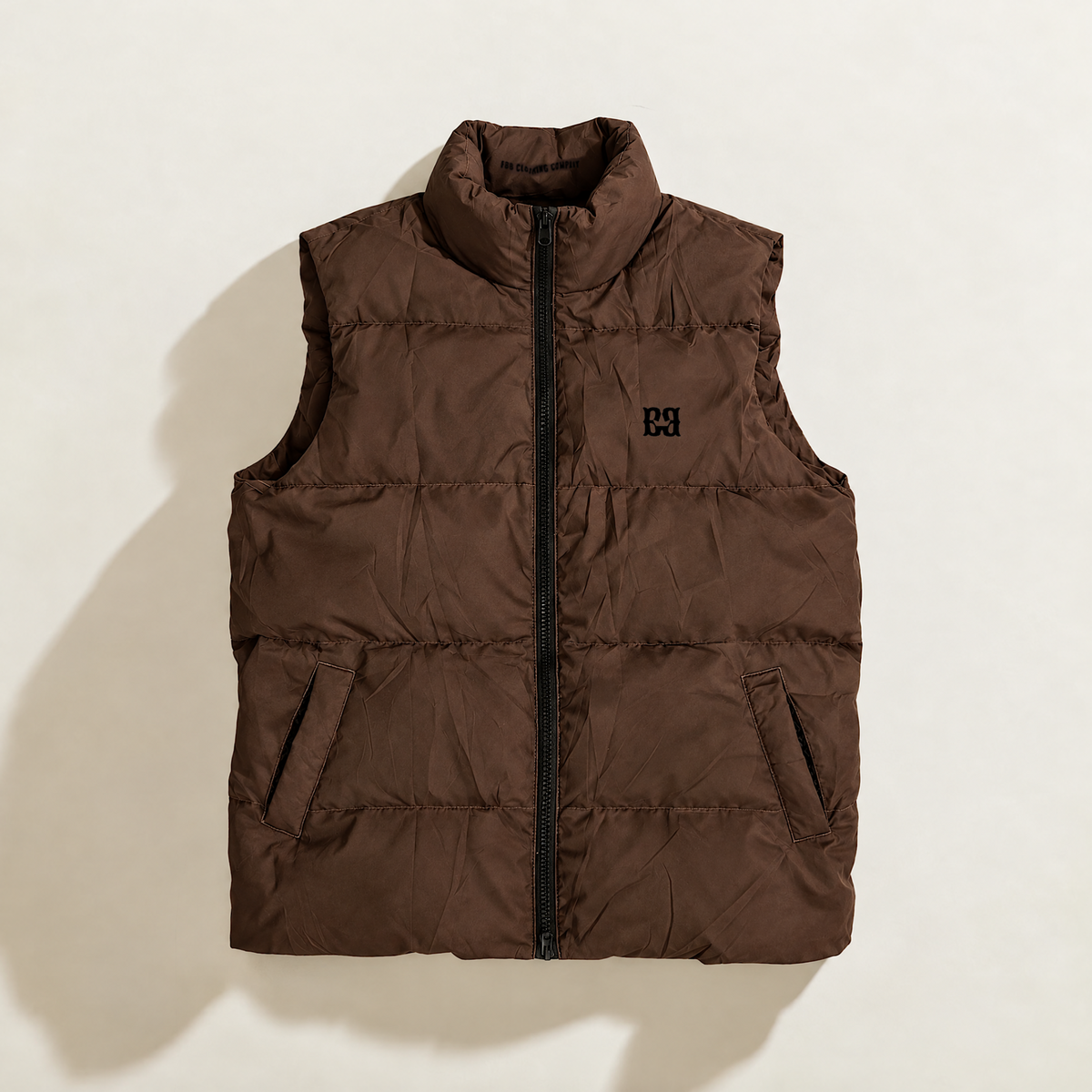 A sleeveless quilted down puffer vest in brown, featuring a black front zipper, a stand-up collar, and a small black logo on the left chest, displayed against a solid white background.