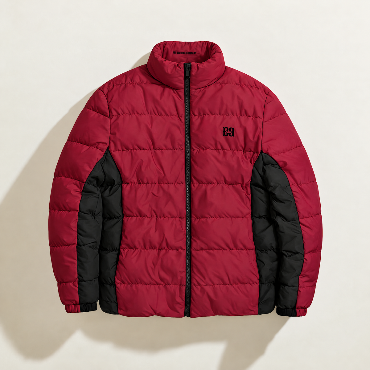 Front view of the burgundy FBB puffer jacket with black side panels, a black zipper and chest monogram.