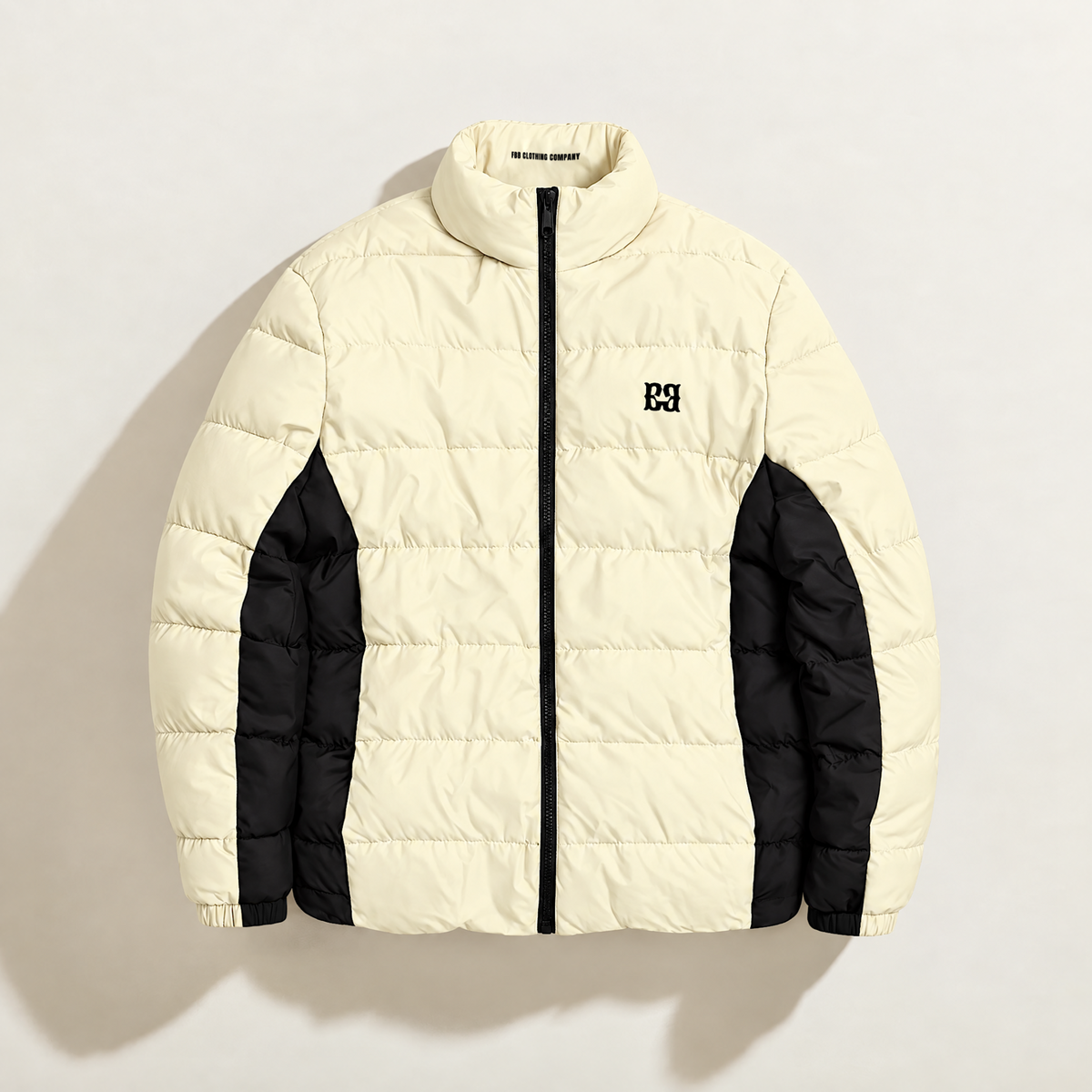 Front view of the cream FBB puffer jacket with black side panels, a black zipper and chest monogram.