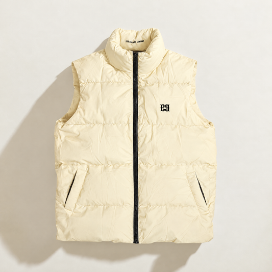 A sleeveless quilted down puffer vest in vanilla cream, featuring a black front zipper, a stand-up collar, and a small black logo on the left chest, displayed against a solid white background.