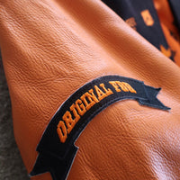 Brown leather jacket with 'Original Fuzz' patch | Varsity jacket with brown, orange, and white design on a gray surface | FBB M3 VARSITY One‑of‑One Collector’s Edition